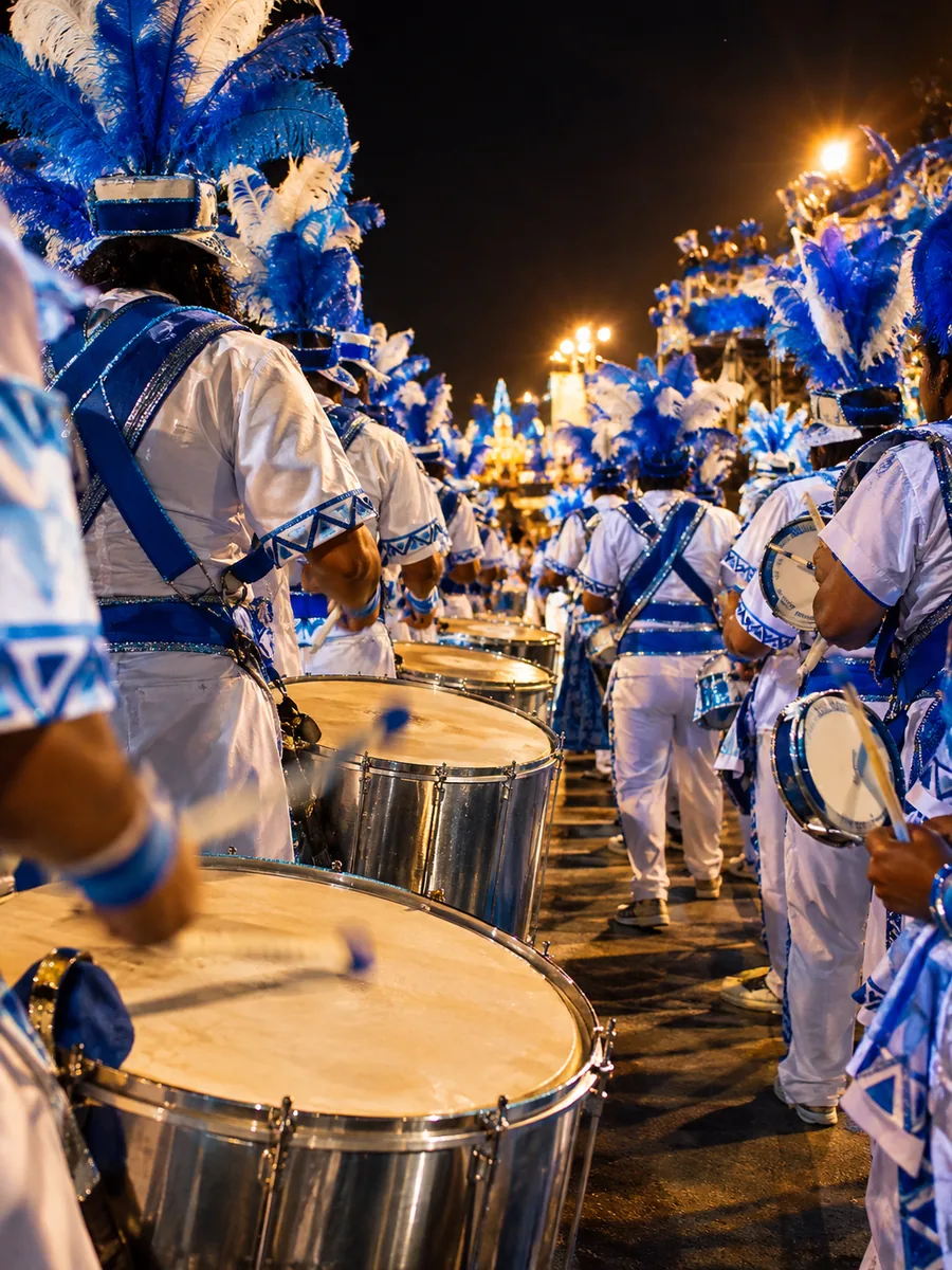A samba school drum section with big silver surdo drums, drummers seen from behind